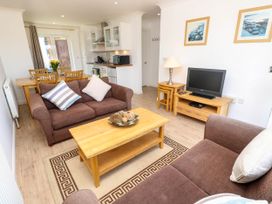 A living room with brown sofas a wooden coffee table and a TV with kitchen and dining area in the background at Cape 12 Near Yarmouth