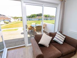 A brown sofa with cushions next to a glass sliding door opening to a patio with a table and chairs overlooking a grassy area with houses at Cape 12 Near Yarmouth