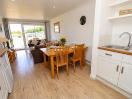 A dining area with wooden table and chairs next to a kitchen sink and a living room with sofas and sliding glass doors at Cape 12 Near Yarmouth