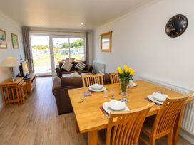 A dining area with a wooden table and chairs set with plates and glasses next to a living room with sofas and a television near sliding glass doors at Cape 12 Near Yarmouth