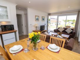 A dining table with yellow flowers in a vase and place settings next to a living room with sofas and a television at Cape 12 near Yarmouth