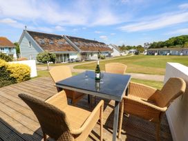 An outdoor patio with a black table and four wicker chairs with buildings and grass in the background at Cape 12 Near Yarmouth