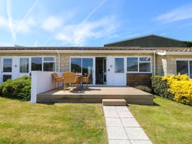 A patio with a wooden deck table and chairs outside a single-story house with sliding glass doors and a paved path leading to the deck at Cape 12 Near Yarmouth