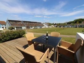 An outdoor patio with a black table and four wicker chairs overlooking a grassy area with row houses at Cape 14 in Yarmouth