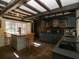 A kitchen with wooden beams on the ceiling wooden chairs around an island and dark cabinets at White Haywood Farmhouse & Barn Craswall