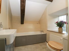A bathroom with a bathtub under a sloped ceiling a sink a toilet with a wooden seat and a window with flowers on the sill at White Haywood Farmhouse & Barn Craswall