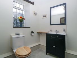 A bathroom with a toilet and wooden seat a window with flowers on the sill a black vanity with sink and mirror and a small wooden shelf on the wall at White Haywood Farmhouse & Barn in Craswall