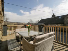 An outdoor patio with wicker furniture a glass table and a vase of flowers overlooking a countryside landscape at White Haywood Farmhouse & Barn in Craswall