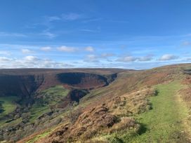 A grassy path on a hillside overlooking a valley with fields and hills under a blue sky at White Haywood Farmhouse & Barn in Craswall