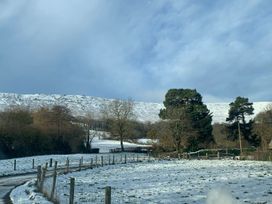 A snow-covered field with fence posts and trees under a cloudy sky at White Haywood Farmhouse & Barn in Craswall