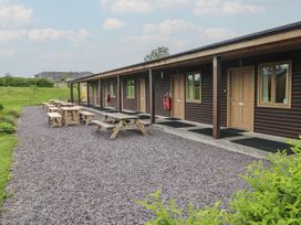 Outdoor area with wooden picnic tables and benches next to a building with multiple wooden doors and windows at Sycamore in Cowbridge