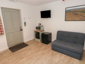 A room with a grey door a small microwave stand a black mini fridge a wall-mounted TV a grey couch and framed wall art at Sycamore in Cowbridge