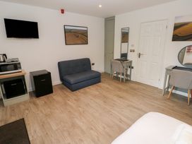 A room with a blue sofa a wall mounted TV a microwave and two desks with chairs at Sycamore in Cowbridge