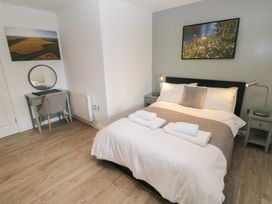 A bedroom with a double bed white linens bedside tables with lamps a desk with a round mirror and a chair at Sycamore in Cowbridge