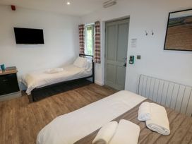 A room with two beds a wall-mounted TV a wooden floor and a door at Beech in Cowbridge
