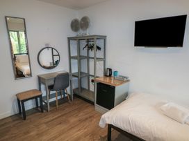 A bedroom with a bed a wall mounted tv a small desk and chair a stool an open wardrobe with hangers two fans on top and a mini fridge at Beech in Cowbridge