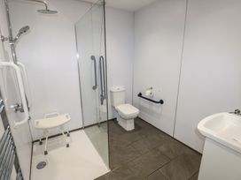 A bathroom with a walk-in shower with a shower chair a toilet with a grab bar and a sink at Beech in Cowbridge