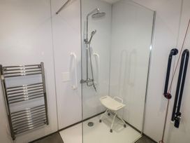 A bathroom shower area with a shower chair grab bars and a heated towel rail at Beech in Cowbridge