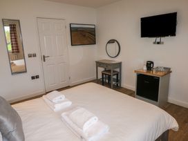 A bedroom with a bed towels a mirror a desk a chair a mini fridge a kettle and a wall-mounted television at Alder in Cowbridge