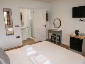 A bedroom with a bed towel stacks a wall mirror a small desk with a round mirror a television and a mini fridge at Alder in Cowbridge