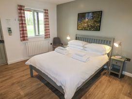 A bedroom with a bed with white linens two bedside tables with lamps a window with plaid curtains and a chair at Cherry in Cowbridge