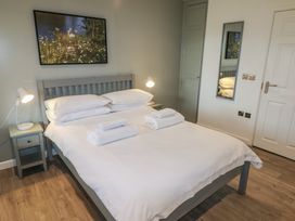 A bedroom with a gray bed frame and white bedding two bedside tables with lamps a wall mirror and a nature painting at Cherry in Cowbridge
