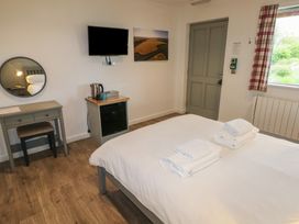 A bedroom with a bed with towels on it a desk with a round mirror a television on the wall a small fridge and a window with plaid curtains at Cherry in Cowbridge