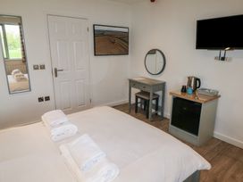 A bedroom with a bed and towels on it a small desk with a mirror a mini fridge with a kettle and cups and a wall-mounted television at Cherry in Cowbridge
