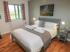 A bedroom with a bed made with white linens gray runner and pillows bedside tables with lamps and a window with red plaid curtains at Chestnut in Cowbridge