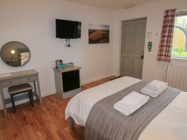 A bedroom with a bed with folded towels a small desk with a stool a wall-mounted TV a kettle on a cabinet and a window with plaid curtains at Chestnut in Cowbridge
