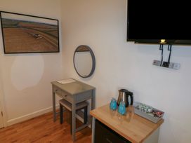 A small room corner with a table and stool under a round wall mirror two blue mugs kettle and a container with coffee pods on a wooden surface below a wall mounted television at Chestnut in Cowbridge