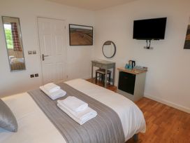 A bedroom with a bed with folded towels a small desk with a stool a mounted TV a small fridge and a wall mirror at Chestnut in Cowbridge