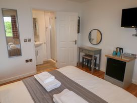 A bedroom with a bed with folded towels a vanity desk with a round mirror a mini fridge a kettle and a wall mounted television at Chestnut in Cowbridge