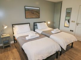 A bedroom with two single beds with white bedding and gray runners a bedside table with a lamp and a wall mirror at Oak in Cowbridge