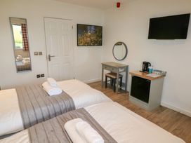 A bedroom with two beds with folded towels a wall-mounted television a small desk with a round mirror a mini fridge and a tea kettle at Oak in Cowbridge