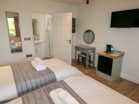 A bedroom with two single beds each with folded towels on top a mirror on the wall a desk with a stool a mini fridge with a kettle and a wall-mounted television at Oak in Cowbridge