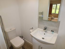 A bathroom with a toilet, a sink with toiletries, and a mirror reflecting a bedroom with a window at Oak in Cowbridge
