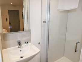 A bathroom with a white sink and faucet a mirror above the sink a glass-enclosed shower with a towel hanging inside and a door in the background at Oak in Cowbridge