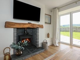 A fireplace with a wooden mantel and a television mounted above it in a room with sliding glass doors and wooden flooring at Criw in Bryncroes near Sarn Meyllteyrn