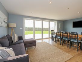 A living room with a sofa and a wooden dining table with chairs by large glass doors at Criw in Bryncroes near Sarn Meyllteyrn