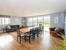 A dining room with a wooden table and black chairs next to a sofa and armchair at Criw Bryncroes near Sarn Meyllteyrn