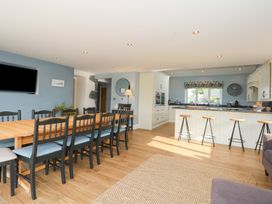 A kitchen and dining area with a long wooden table and black chairs and a kitchen island with bar stools at Criw in Bryncroes near Sarn Meyllteyrn
