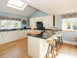 A kitchen with white cabinets black countertops wooden stools under a counter and windows with floral valances at Criw in Bryncroes near Sarn Meyllteyrn