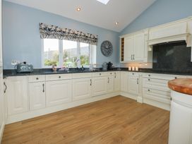A kitchen with white cabinets black countertops wooden floor and a window with floral curtain at Criw in Bryncroes near Sarn Meyllteyrn