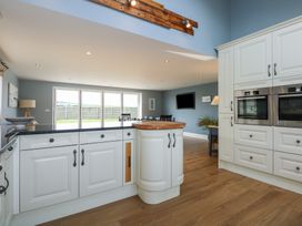 A kitchen with white cabinets a black countertop wooden floor and a dining area with chairs and large windows at Criw in Bryncroes near Sarn Meyllteyrn