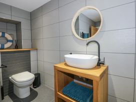 A bathroom with a toilet and a wooden vanity with a white sink and round mirror at Criw in Bryncroes near Sarn Meyllteyrn