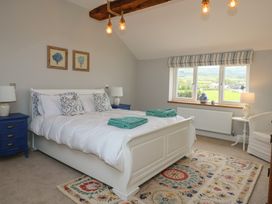 A bedroom with a white bed and blue bedside tables with lamps a window with vases on the sill and a colorful rug on the floor at Criw in Bryncroes near Sarn Meyllteyrn