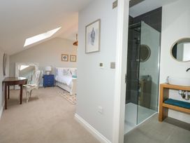 A bedroom with a bed bedside table chair desk and skylight next to a bathroom with a glass shower and sink at Criw in Bryncroes near Sarn Meyllteyrn