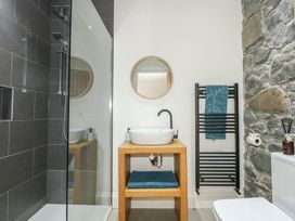 A bathroom with a walk-in shower with gray tiles a wooden vanity with a white vessel sink and round mirror a towel warmer with a blue towel and a stone wall at Criw Bryncroes near Sarn Meyllteyrn