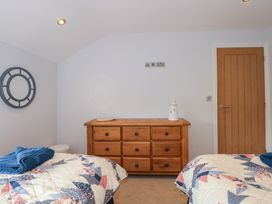 A bedroom with two beds with patterned quilts a wooden dresser a round wall mirror and a wooden door at Criw in Bryncroes near Sarn Meyllteyrn